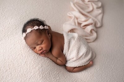 newborn girl wrapped in white fabric with a cream color headband by Maryland newborn photographer