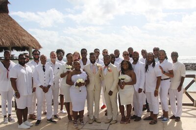 A group of elegantly dressed individuals in white suits and ties, celebrating a destination wedding in a picturesque setting.