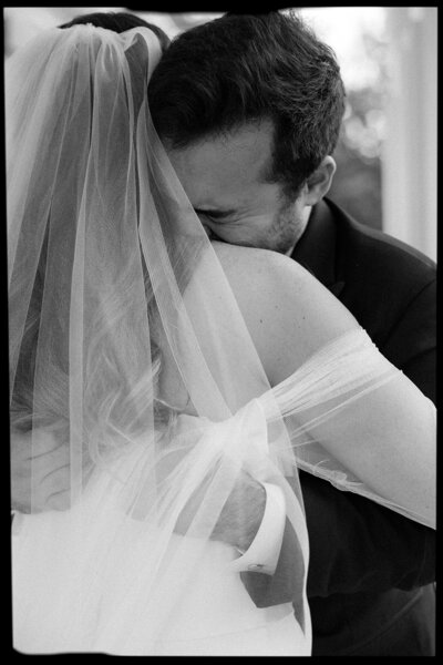 Groom emotionally embraces bride during her wedding vows on their wedding day.