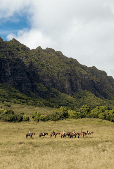 Men on horseback under mountain range in Hawaii
