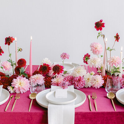 A centrepiece of bold pink and red flowers on a table with a bright tablecloth.