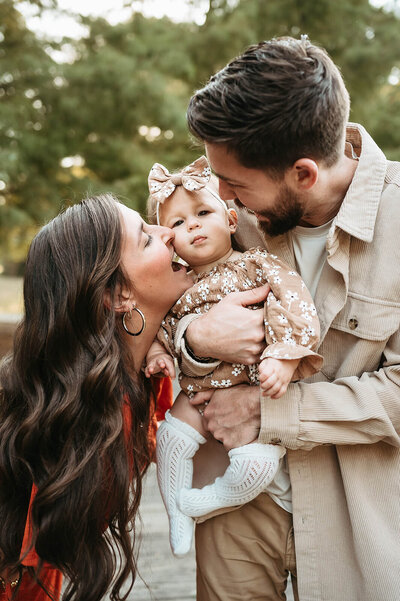 Candid family photo by Charlotte photographer—parents kiss baby during golden hour.