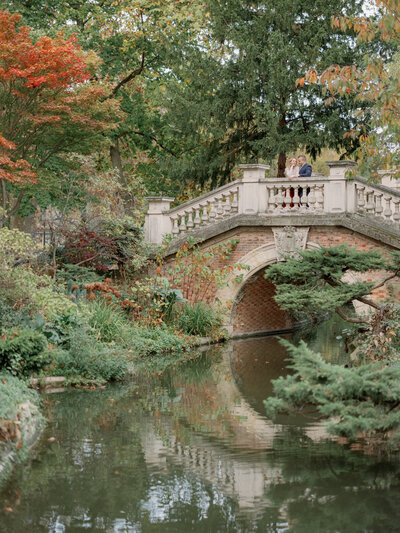 a couple standing on a bridge in parc monceau in paris with autumn leaves  all around