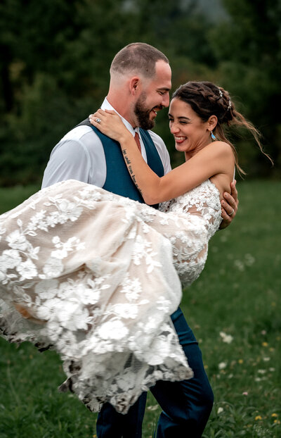 A groom with his bride spinning her around in a field in the adirondack mountains