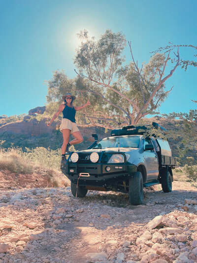 Buzz, standing on the bull bar of her Hilux thats shes travelling around Australia in with a big beautiful gumtree and Aussie outback behind her