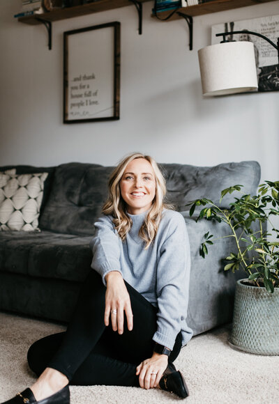 woman sitting on the floor while leaning against a couch while smiling