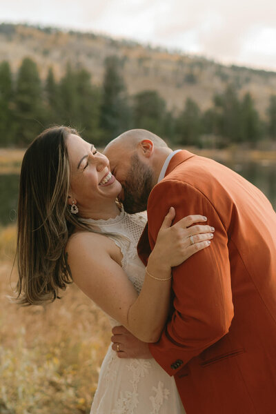couple laughing and smiling at each other during their adventure session on a mountain top