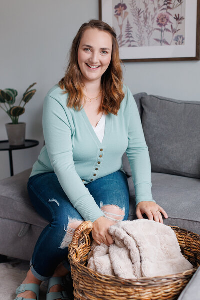 Emily smiling, sitting on a couch placing a folded blanket into a basket