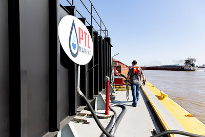 Branding photograph of a man walking along a barge with the company sign in the foreground and the river in the background.