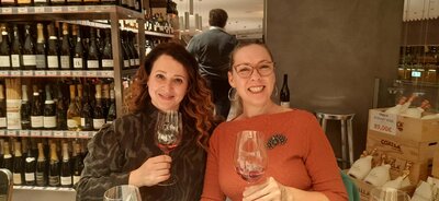 Cristina and guest each holding a glass of red wine and smiling during a wine tasting.