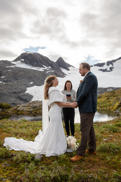 A bride and groom stand facing each other holding hands while Becky officiates their wedding ceremony in Alaska.