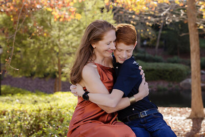 Cozy autumn portrait of mom and son seated together on park bench surrounded by fall foliage at Ballantyne Corporate Park