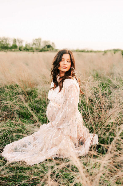 Springfield MO maternity photographer captures pregnant mom kneeling in field holding belly