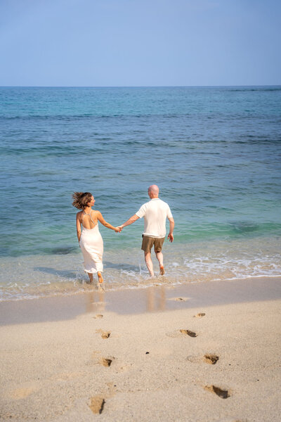 Couple holding hands, walking into the ocean, by Hawaii engagement photographer