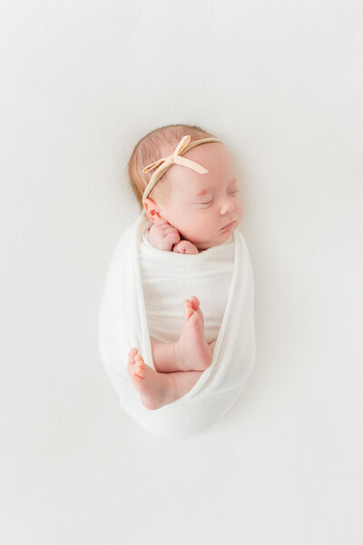 A baby girl swaddled with her feet sticking out on a white blanket by Northern Virginia Newborn Photographer