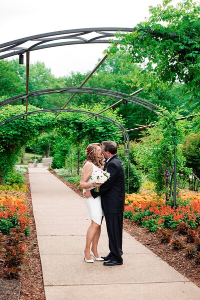 Couple sharing a kiss under an floral arbor at Cheekwood for an elopement photoshoot