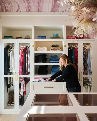 Organizing a women's walk-in closet with open shelving and glass doors for hanging