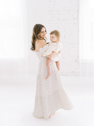 mom holding toddler girl smiling at her in white studio with their louisville family photographer