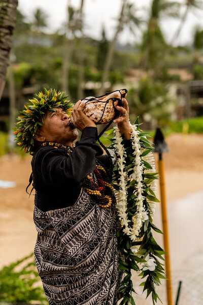 wedding officiant blowing conch shell at the start of a Maui wedding