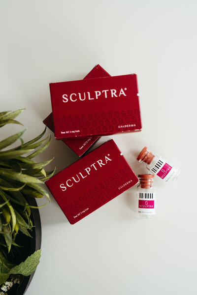Flatlay of Sculptra biostimulator vials and boxes surrounded by greenery