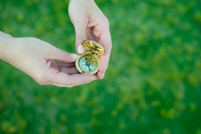 woman holding an open compass with green grass in the background