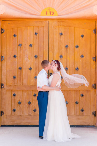 husband and wife kiss in front of church doors