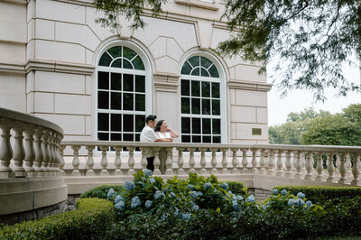 Groom holds the brides dress train as they go up some steps