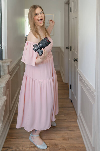 Photographer Melissa Driggers with in pink dress holding her camera and laughing