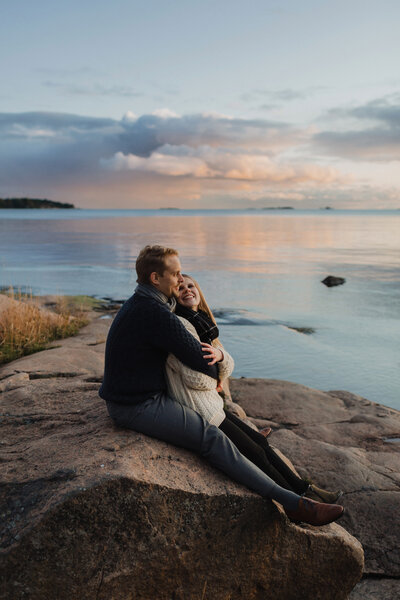 Pari istuu rantakalliolla auringonlaskun aikaan syksyllä Lauttasaaressa Helsingissä