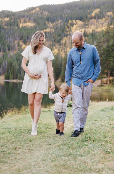 A happy toddler walks with mom and dad holding hands along a lakeside trail