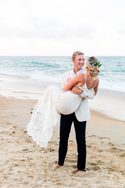 groom holding bride on the beach