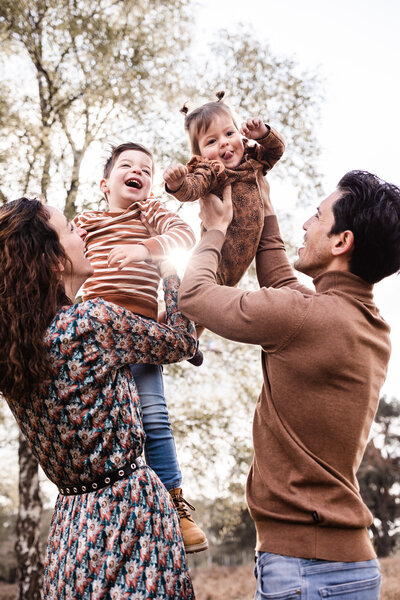 Gezinsshoot op de venlose heide papa en mama houden kindjes zoon en dochter in de lucht met zon op achtergrond