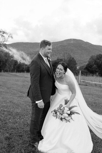 A black and white photo of a bride and groom. The bride is laughing and there are mountains in the background.