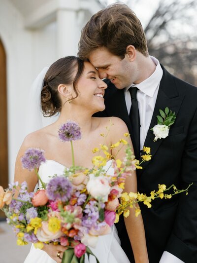 Joyful wedding portrait of a bride and groom sharing a tender moment, captured with vibrant florals and natural emotion.