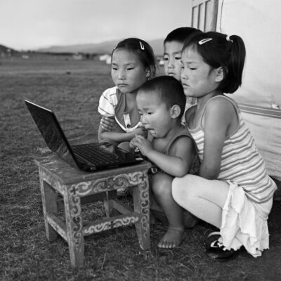 Asian children looking at laptop in a field highlighting digital poverty