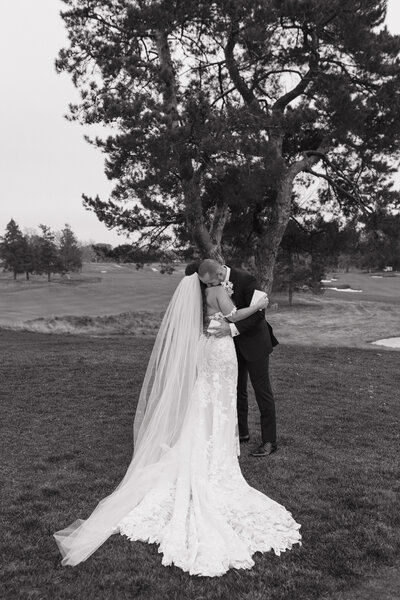 bride and groom embracing while standing outside with a large tree in the background