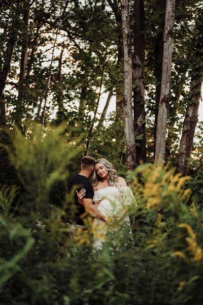expectant mom and dad snuggled amidst late summer foliage