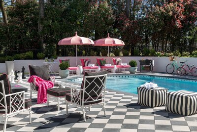 Vibrant backyard pool area with pink umbrellas, black and white checkered patio, and custom outdoor furniture, designed for stylish outdoor living in Little Rock, Arkansas by Better Lawns and Gardens.