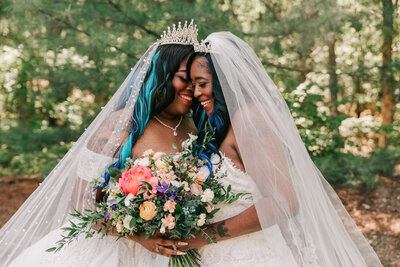 two brides posing together for wedding photos at a woodsy outdoor venue, captured by Ari Marie Photography, a Boston alternative wedding photographer