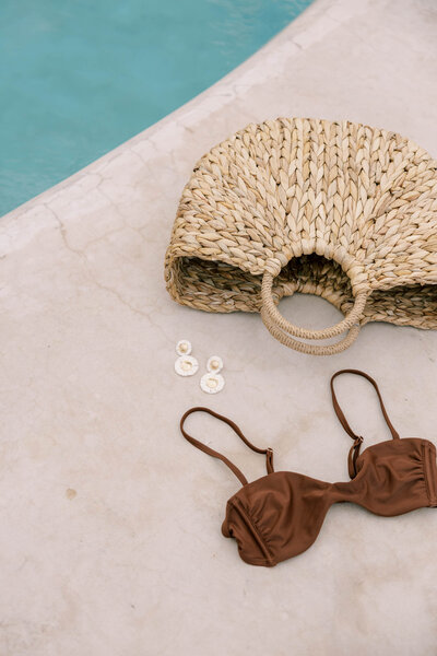 Straw beach tote, earrings and bikini next to luxury pool