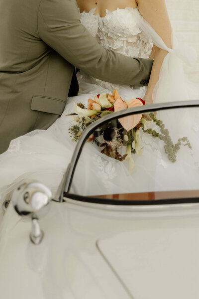 Groom holds bride's hand as they drive off in their 'Just Married' vintage car.