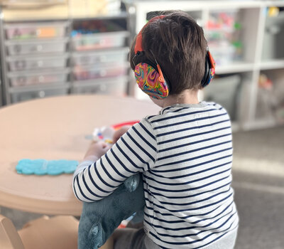 Photo from the back of a little boy wearing a striped shirt and wearing headphones while playing a learning game