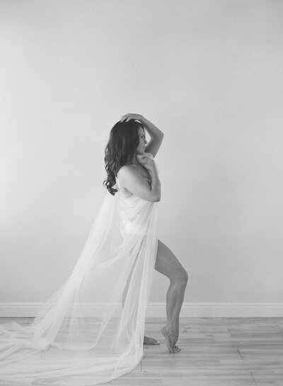 A woman with a veil draped around her body poses for boudoir photos in Denver.