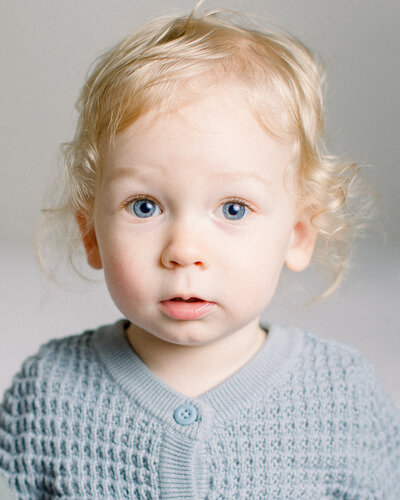baby with curly blonde hair and blue eyes in a blue knit sweater, by NH newborn photographer Fieldstone Studio