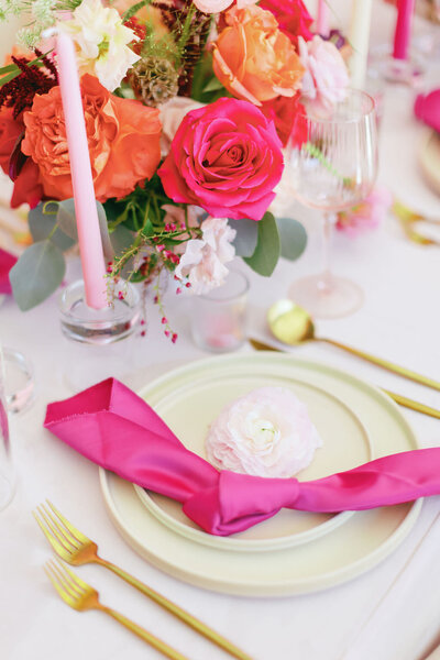 Table setting with pink napkin, gold silverware, pink candles, and a pink and orange floral centerpiece