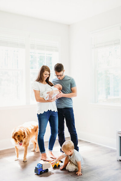 parents holding newborn with toddler and dog around