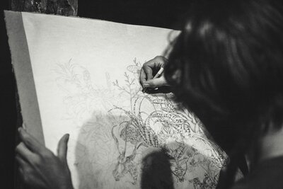 Black and white image of an artist sketching details closely.