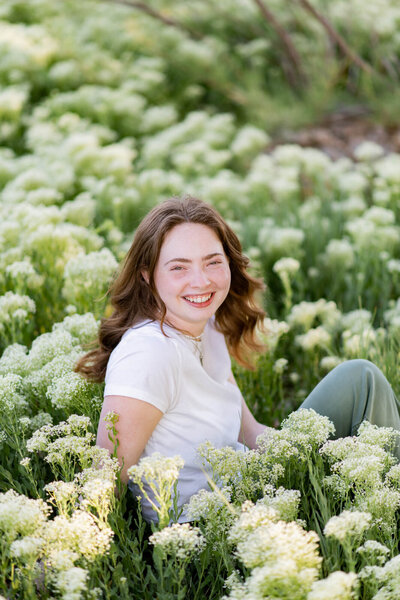 Girl is smiling at the camera while sitting in a field of flowers