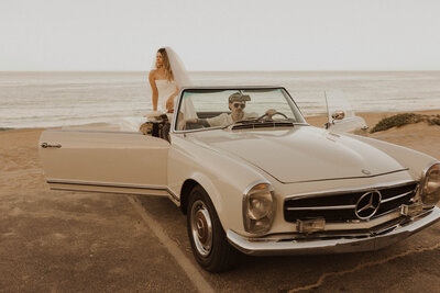 bride and groom sitting in a classic car on beach