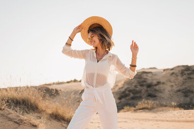 stylish-happy-attractive-smiling-woman-posing-desert-sand-dressed-white-clothes-wearing-straw-hat-sunglasses-sunset